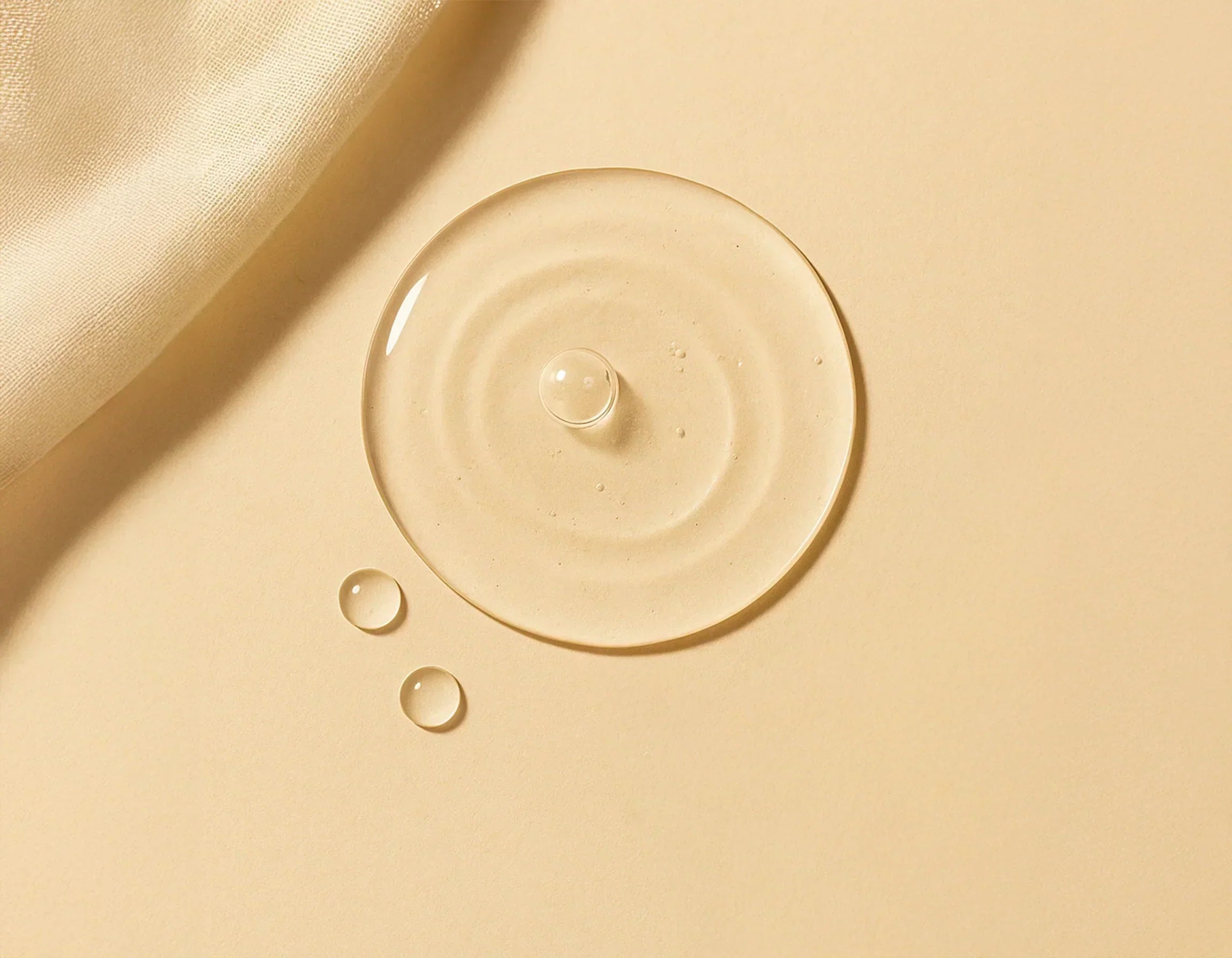 A clear droplet of hyaluronic acid resting on a warm beige surface beside aloe leaves, symbolizing deep hydration and purity – Suvera Self Care