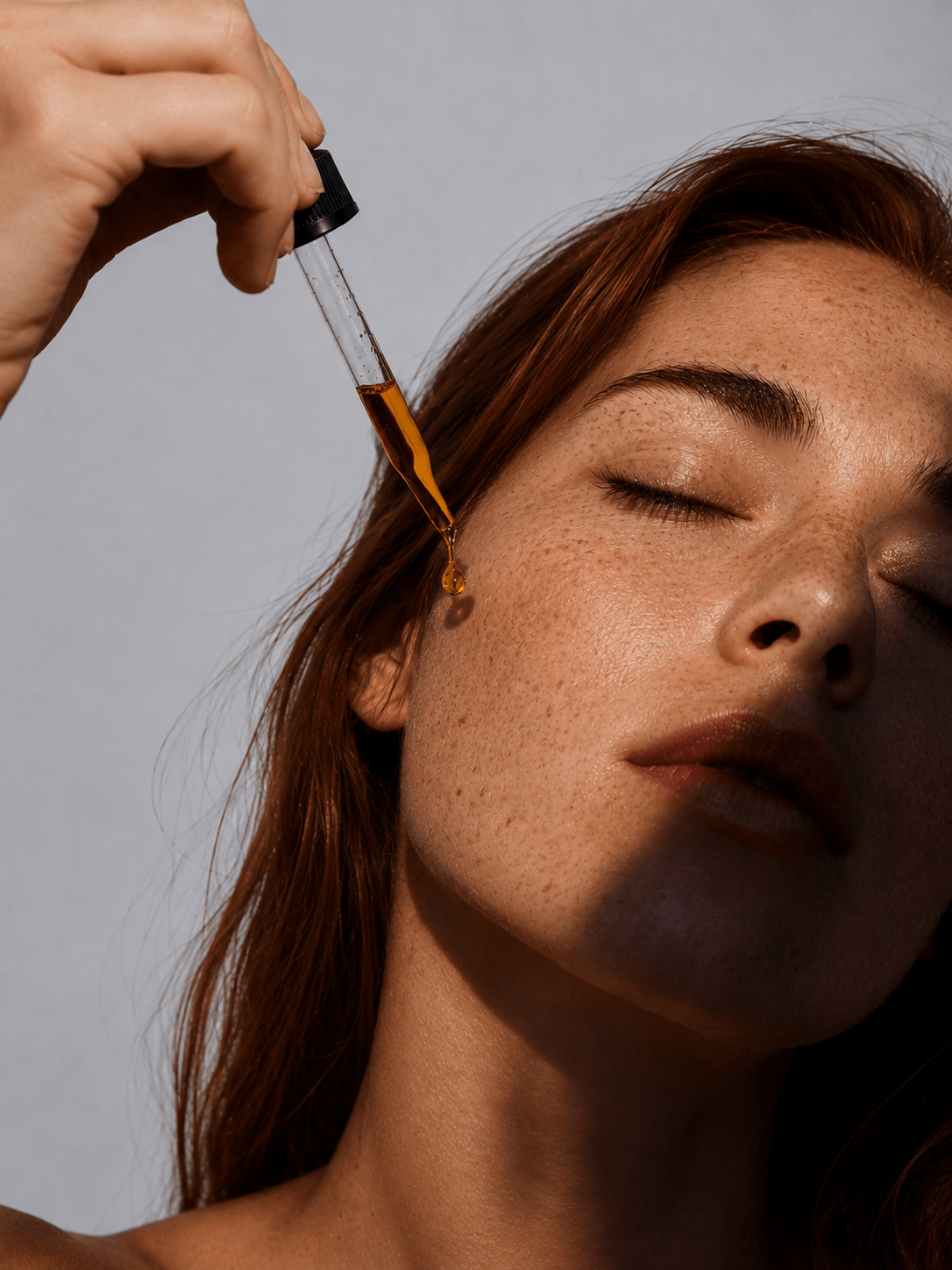 Person applying a dropper of oil to their skin against a neutral background - modern skincare ritual by Suvera Skincare