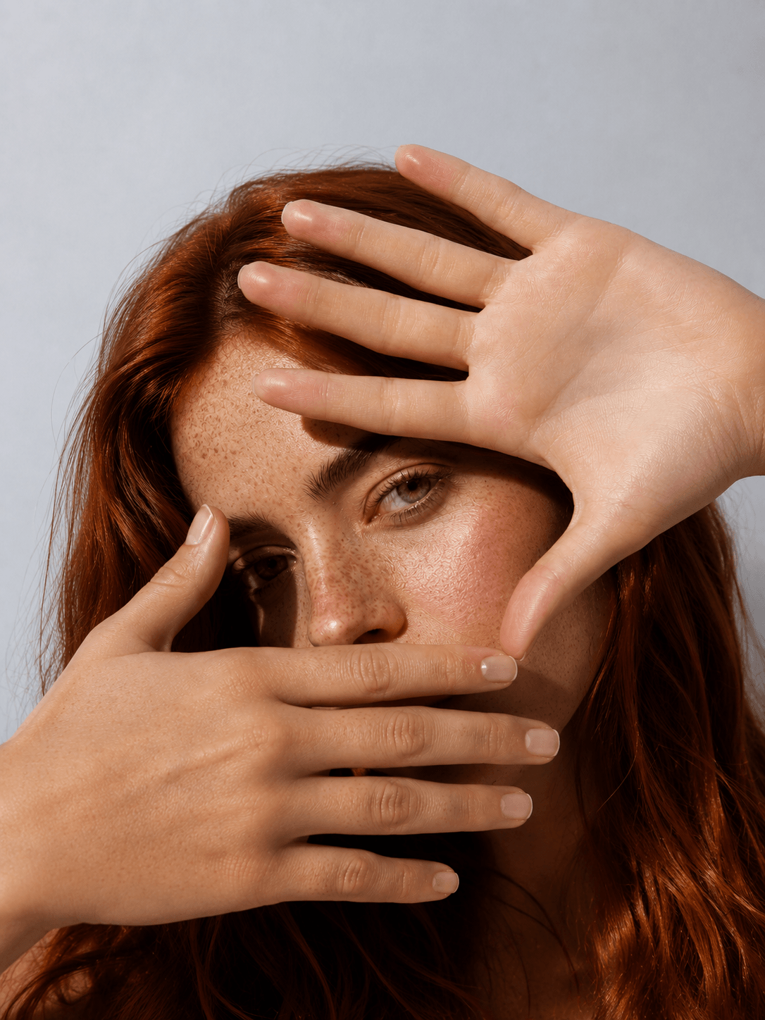 Woman with red hair covering her face with her hands against a gray background - Suvera Skincare clean beauty essential