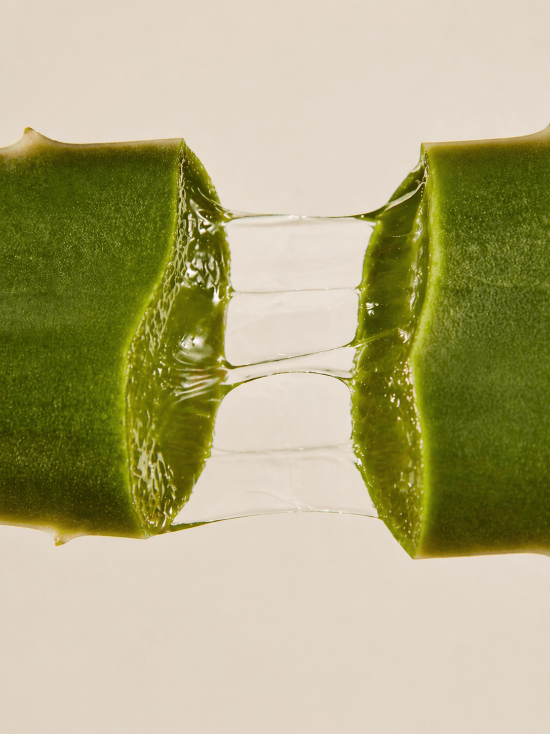 Close-up of aloe vera gel being squeezed from a leaf on a beige background