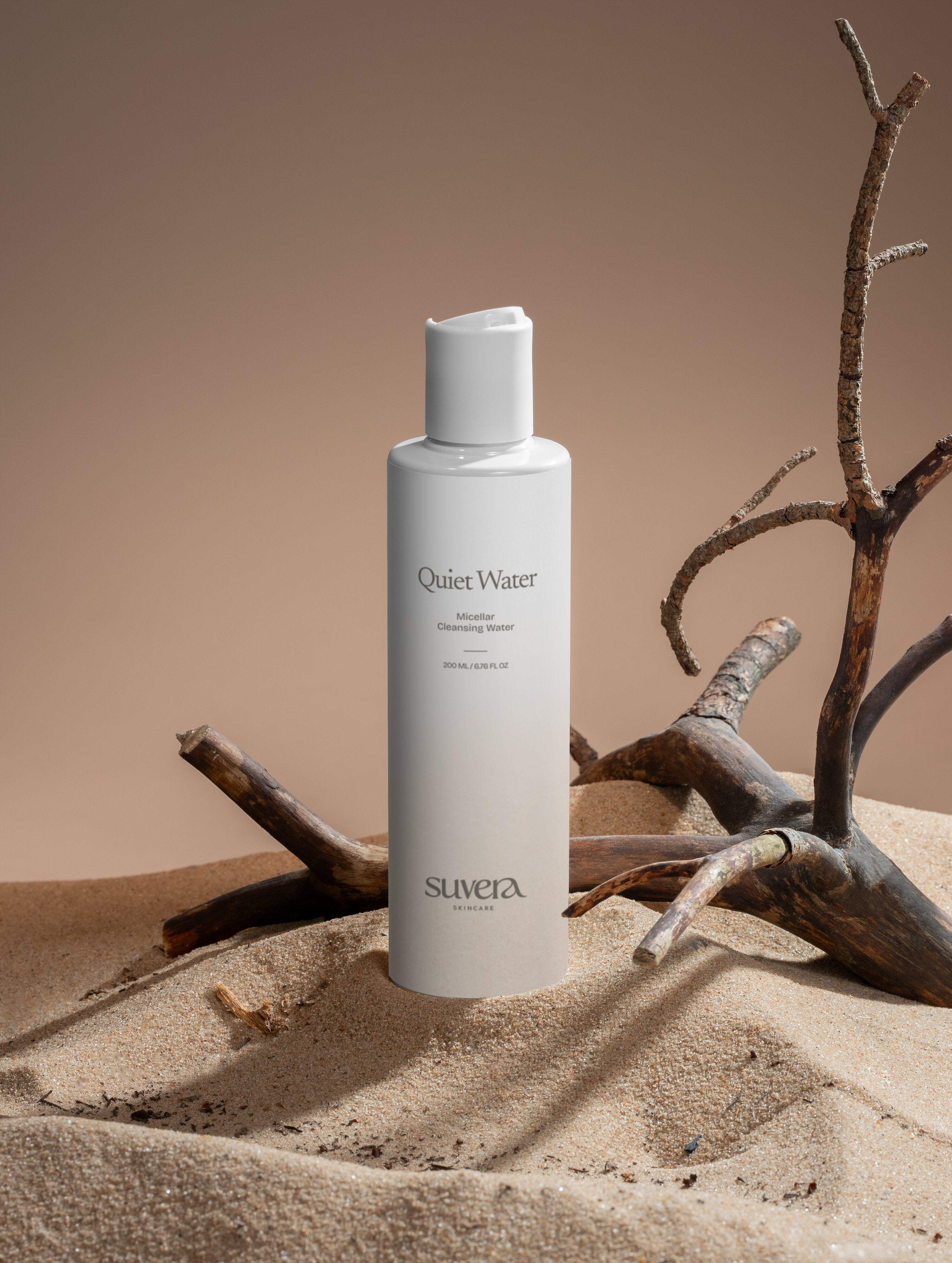 White bottle labeled 'Silveta' on a sandy surface with branches. Suvera Skincare, Bureau Veritas certified, vegan skincare